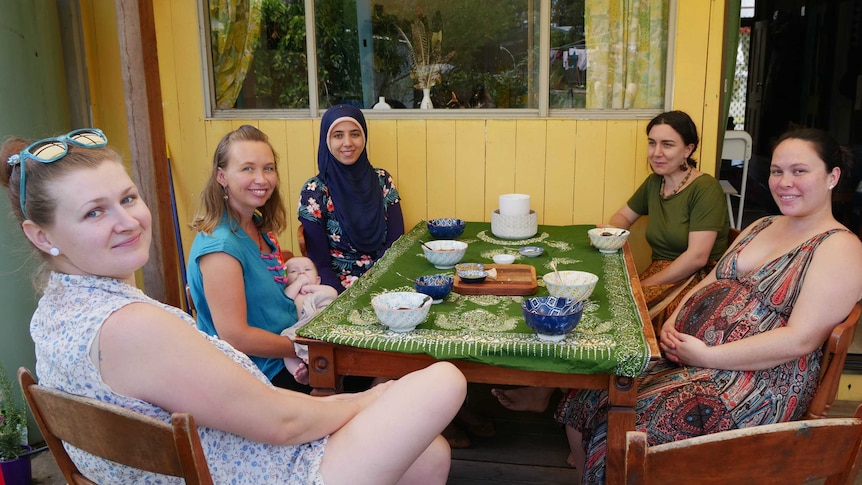 A group of women and a baby around a table set with bowls of soup smiling to camera