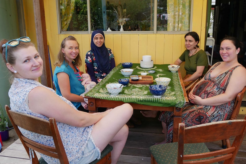 A group of women and a baby around a table set with bowls of soup smiling to camera