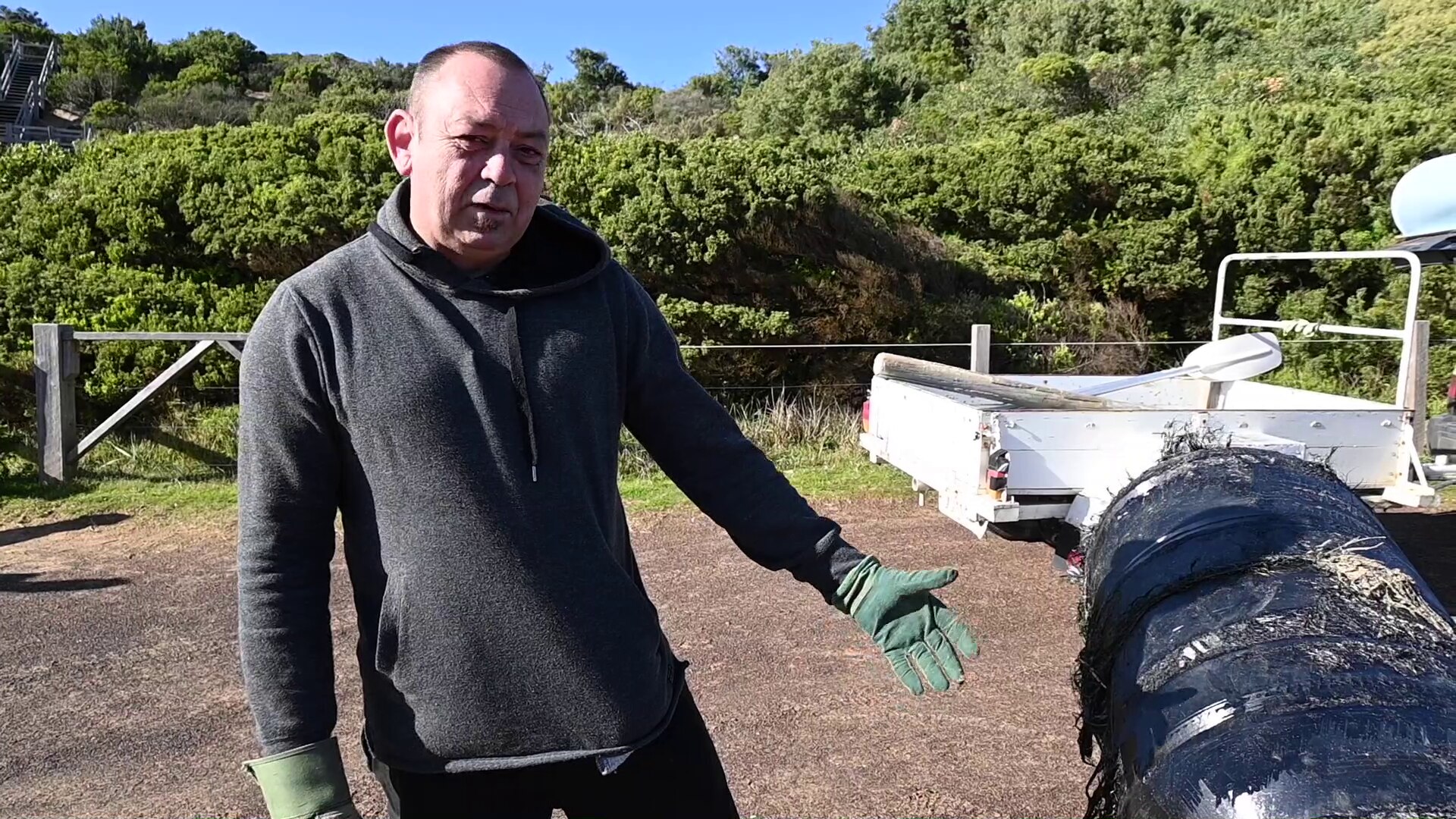 A man wearing green leather gloves stands next to a black cylinder