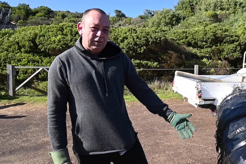 A man wearing green leather gloves stands next to a black cylinder