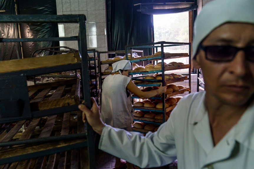 A woman pulls a cart while another loads bread onto shelves