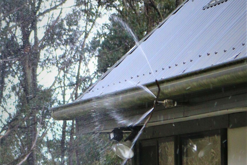 Roof-based water sprinkler spraying over a house.