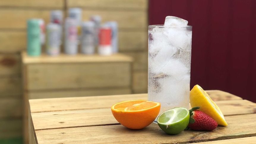 A glass of hard seltzer with cans of seltzer in the background