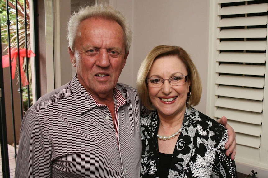 Conrad and Mandy Whitlock pose for a photo together at their house, they are both dressed up and smiling.