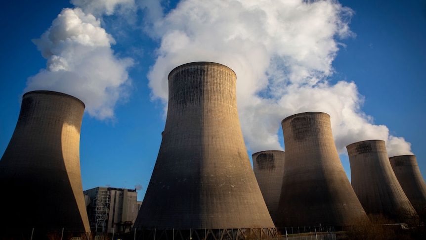 White smoke billows from the top of a row of giant chimneys at a coal-fired power station.