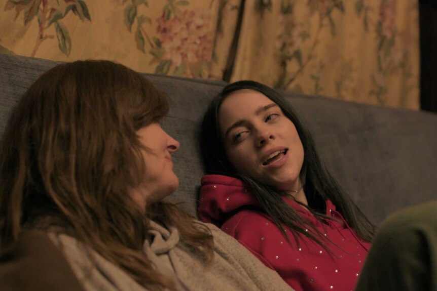 A scene from the documentary Billie Eilish: The World's a Little Blurry with Billie and her mother Maggie sitting on a couch