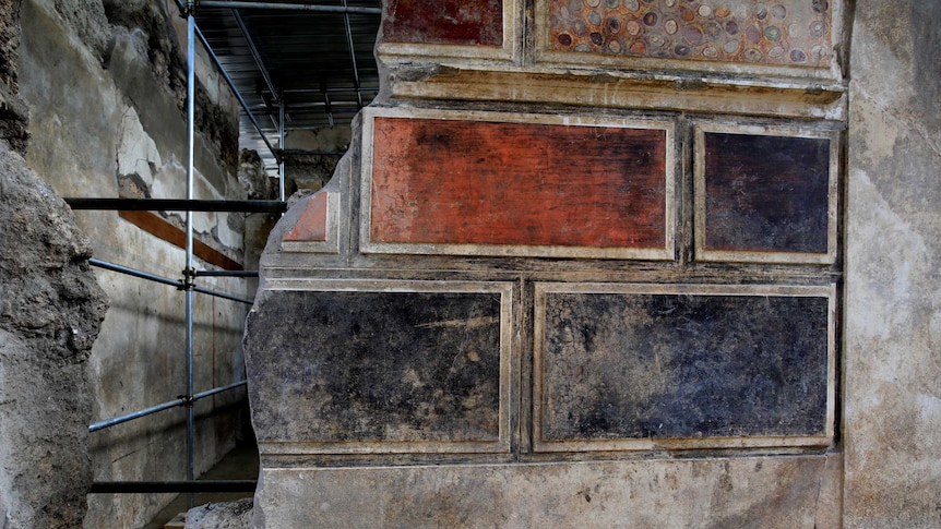 A wall reveal brightly coloured paintings on a wall that are being cleaned up