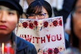 A woman holds a sign at a protest reading: "With You"