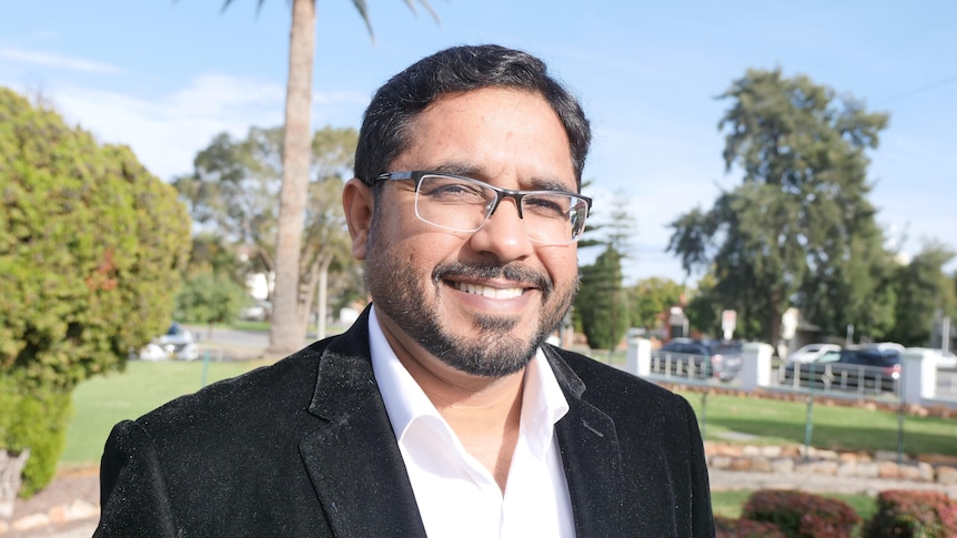 A man wearing glasses standing in a park.