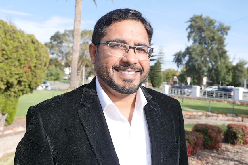 A man wearing glasses standing in a park.