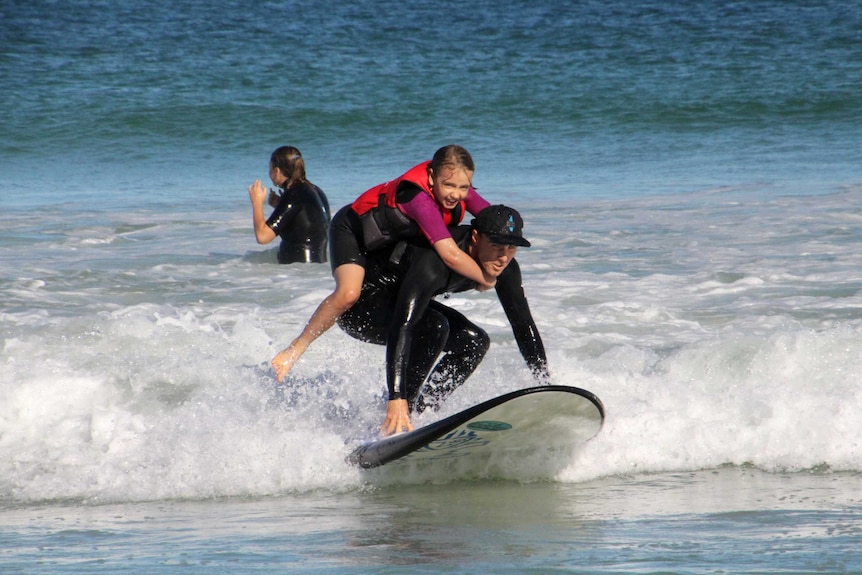 A man rides a surfboard with a girl on his back.