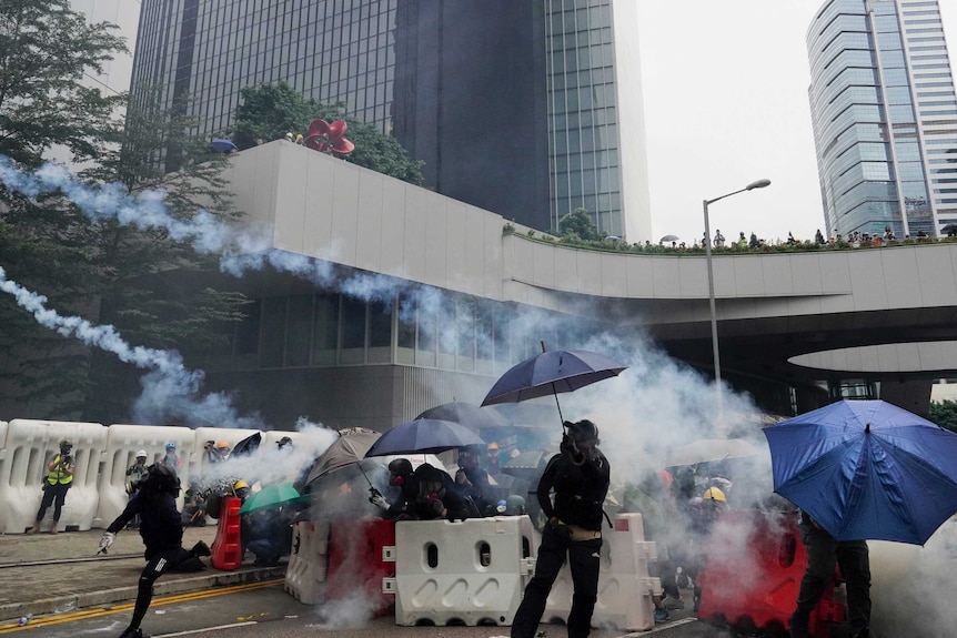 Protesters having tear gas thrown at them, using umbrellas to shield themselves
