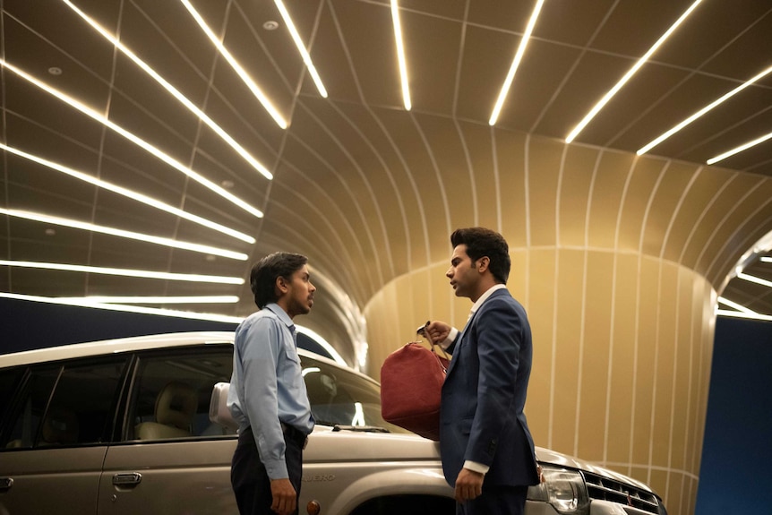 A still from the film The White Tiger with a rich businessman (Rajkummar Rao) handing a bag to his driver (Adarsh Gourav)