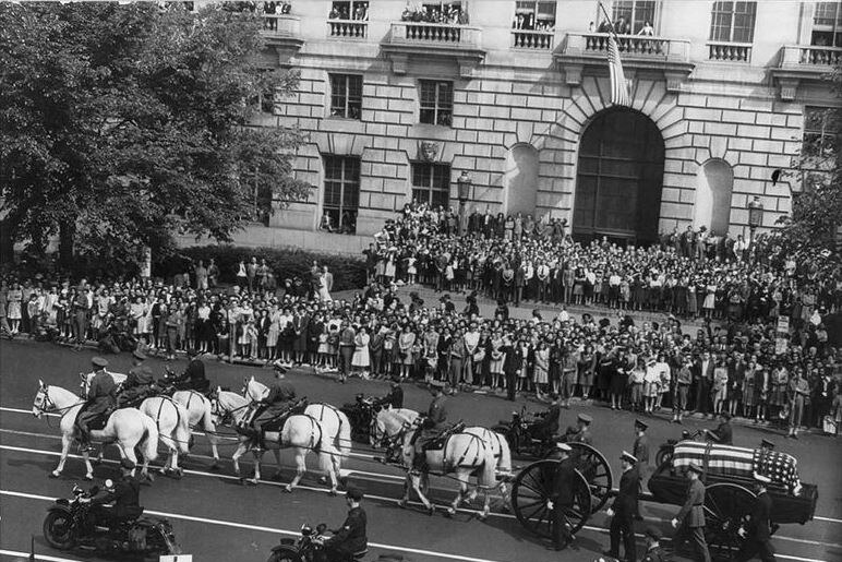 Black and white photo of Franklin Roosevelt casket carried by horse-drawn carriage passes by people on the street