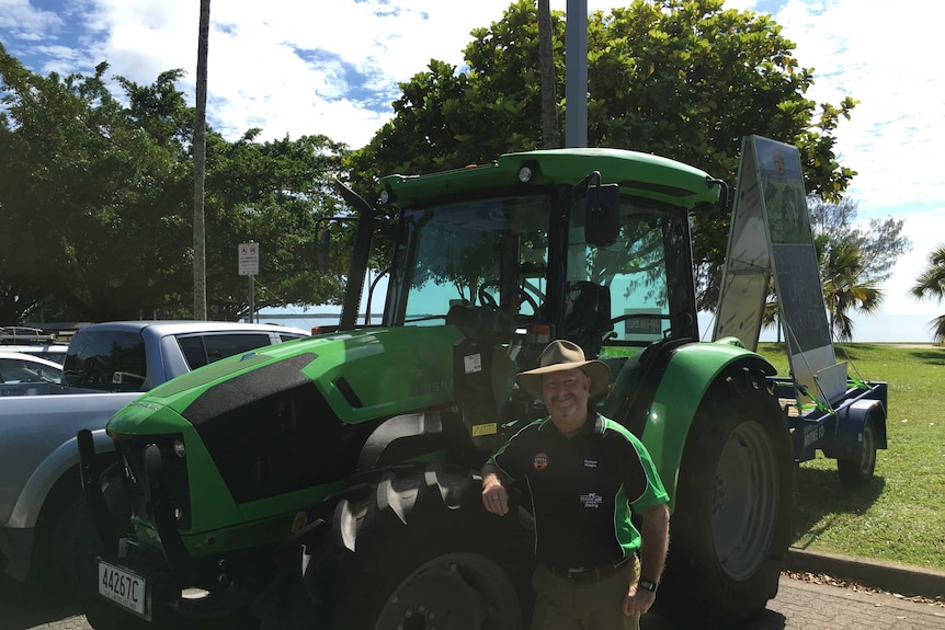 Farmer Greg Dennis standing beside a bright green tractor on Cairns esplanade