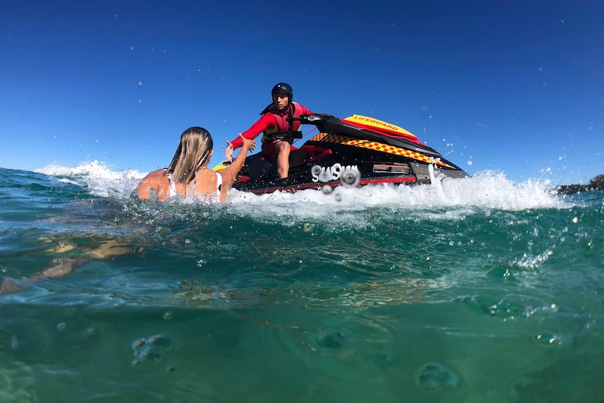 a man riding a jet ski stretching his hand to a woman in the surf