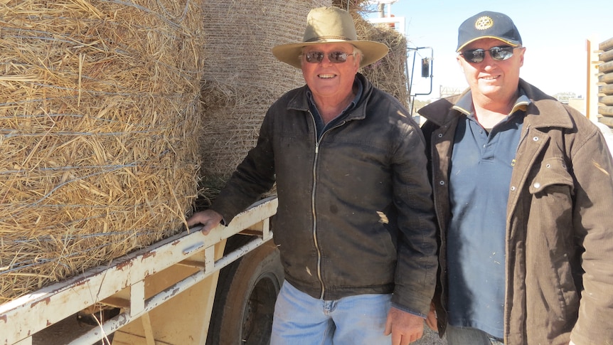 Warwick Champion and David Neal from Longreach Rotary stand beside a truckload of hay bales