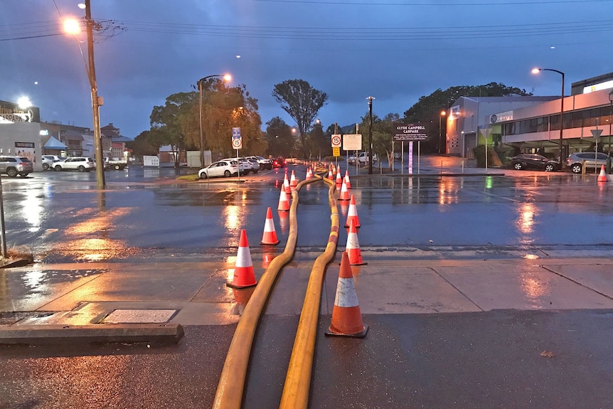 A street at night with two yellow pipes and red cones