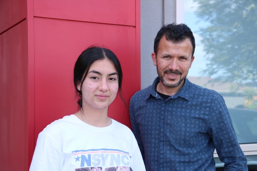 A teenager and a man stand in front of a red wall