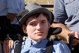 Harrison Creevey wears a felt hat and sits in a wheelchair.