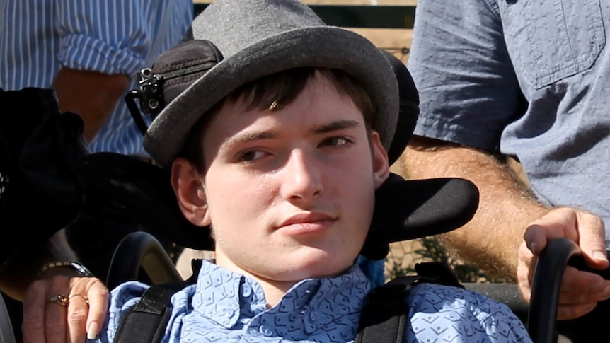 Harrison Creevey wears a felt hat and sits in a wheelchair.