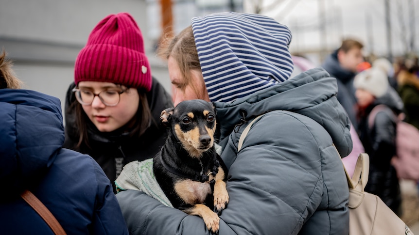 a group of women wearing winter clothes huddle together with one of the women holding a small dog in her arms 