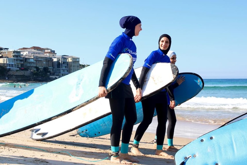 Three women wearing burkinis and holding surfboards on a beach
