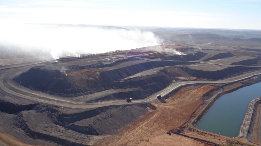 Large smoke plumes can be seen rising from a waste rock pile.