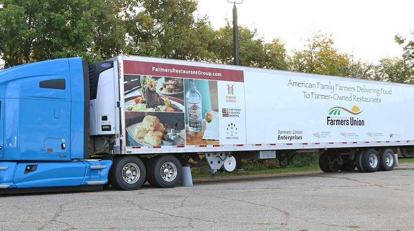 A semi trailer with a bright blue cab and restaurant images and a Farmers Union logo on the trailer.