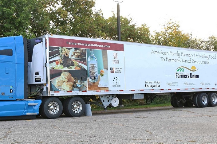 A semi trailer with a bright blue cab and restaurant images and a Farmers Union logo on the trailer.