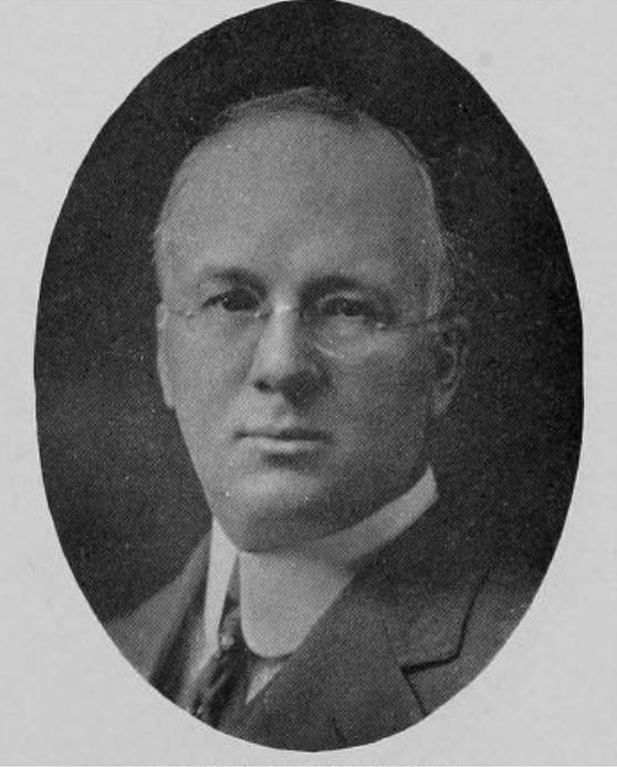 Black and white portrait of a middle-aged man with glasses and light eyebrows and hair.