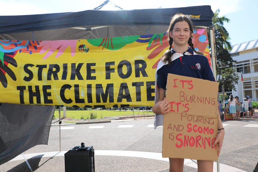 A girl wearing a school uniform holding a sign reading 'it's burning it's snoring and scomo is snoring'