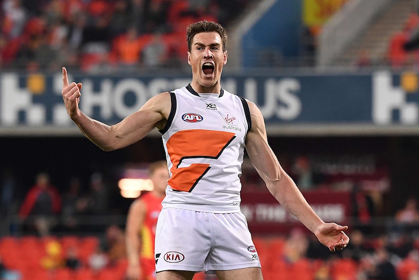 A male AFL player screams out and points a finger on his right hand as he celebrates kicking a goal.