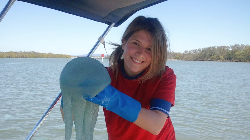 Woman holds a large blue jellyfish while on a boat on a river.