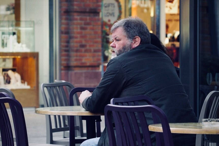 A man sits at a table outside a shop in Workington.