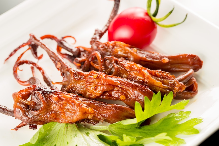Duck tongues are placed on a plate - they're long, ending in tentacle-like pieces and served glazed with a salad on the side 