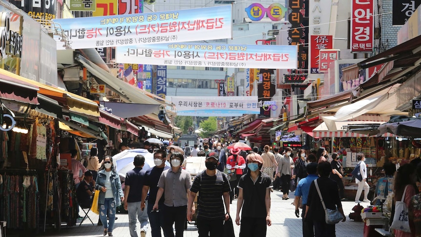 A crowd of people wearing masks while walking through a shopping strip