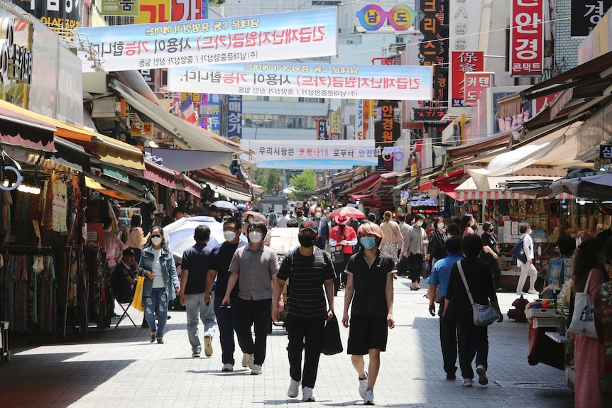 A crowd of people wearing masks while walking through a shopping strip