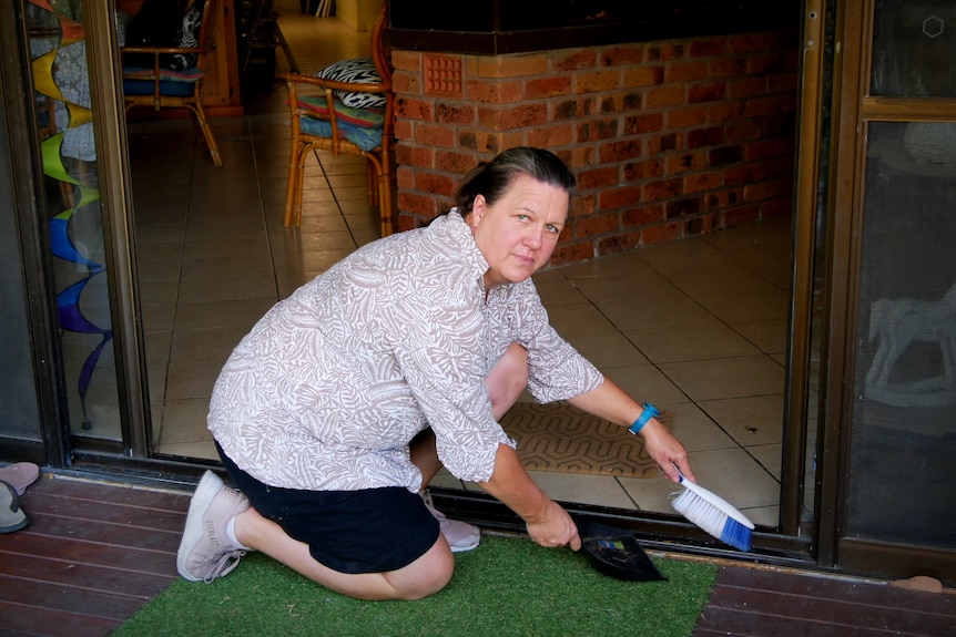 A woman uses a dustpan and brush to sweep dead ants from the doorframe of a home
