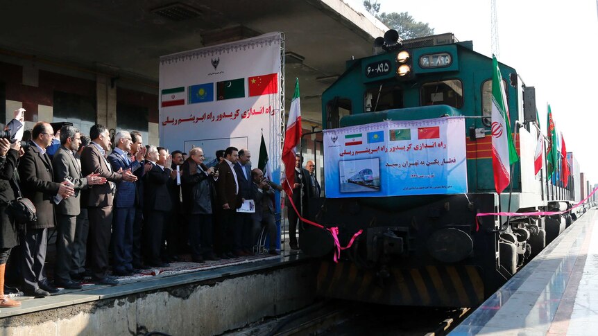 Iranian officials applaud on the platform as the train arrives.