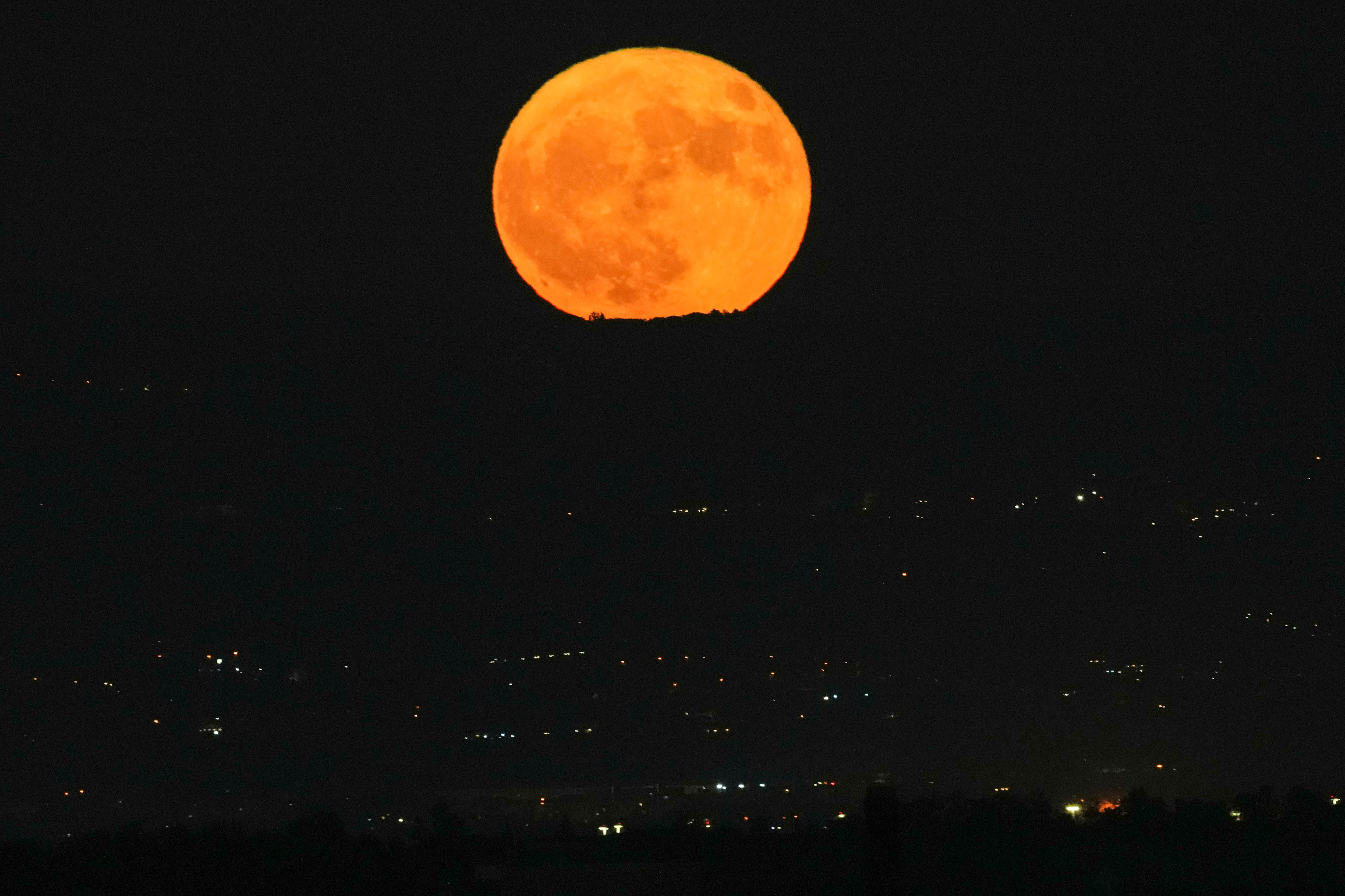 A large orange moon rises above a dimly seen cityscape.