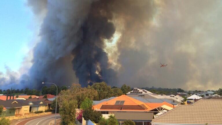 Houses in Atwell are seen against plumes of smoke from a bushfire