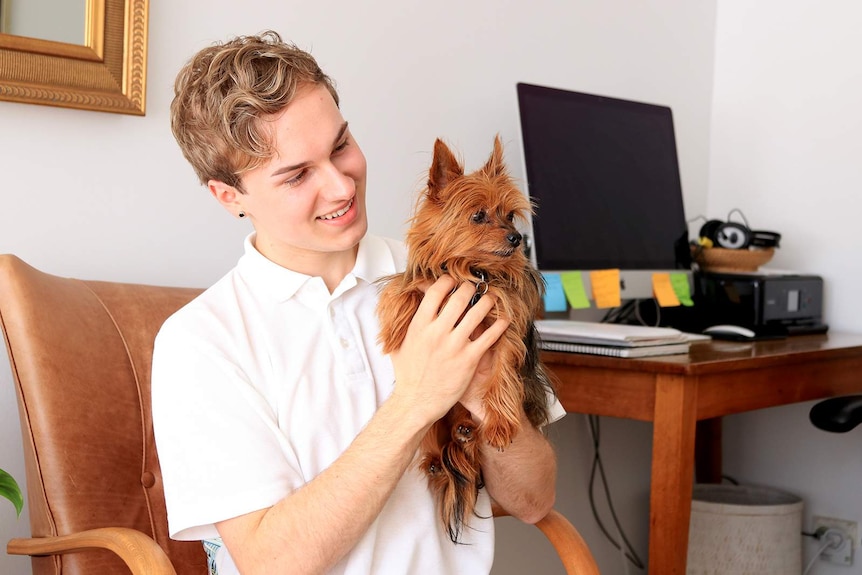 Blake Douglas holds his dog while sitting in a chair near his computer.