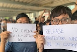 Two young Hong Kong men are shown close up with white A4 signs covering the bottom two-thirds of their faces.