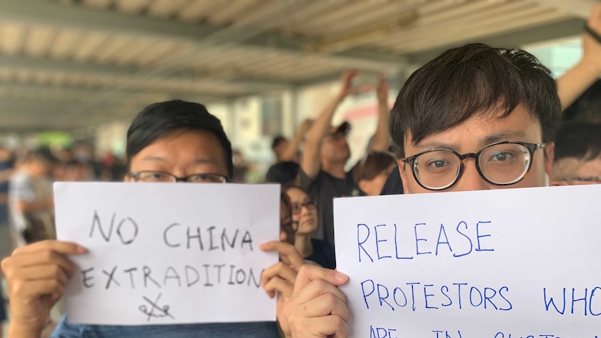 Two young Hong Kong men are shown close up with white A4 signs covering the bottom two-thirds of their faces.