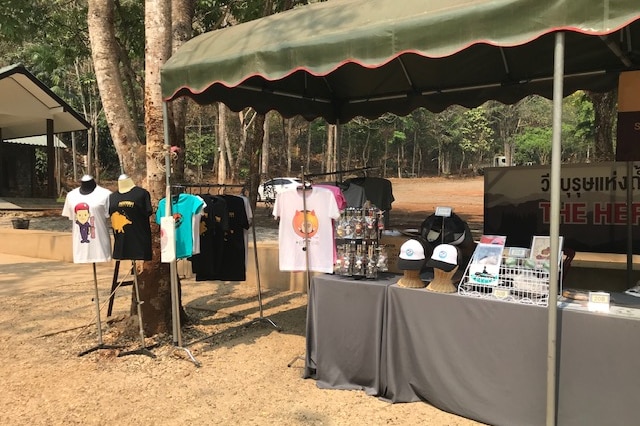 A stall with T-shirts, caps and small keepsakes under a green tarpaulin.