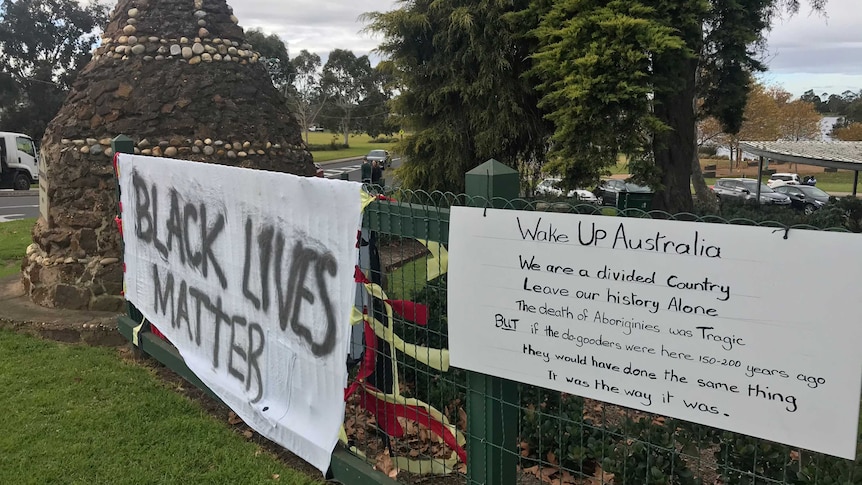 A historical monument with two signs erected near it. One is in favour of the Black Lives Matter movement