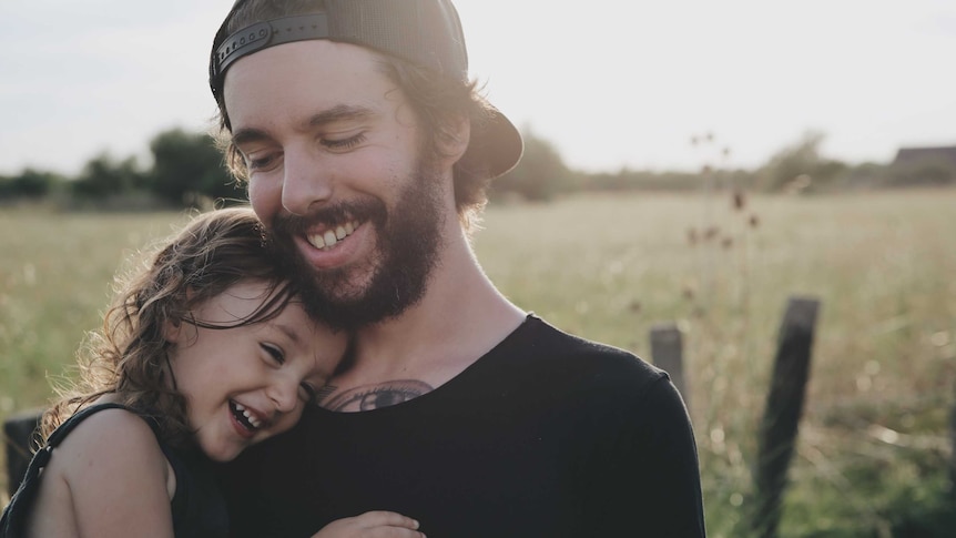 A father and his toddler daughter cuddle in a backyard, in a story about co-parenting tips during the pandemic.