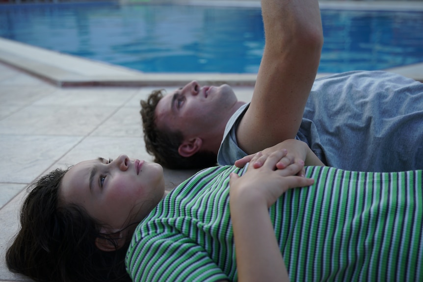 一个 12 岁的女孩和一个 20 多岁的男人躺在游泳池边