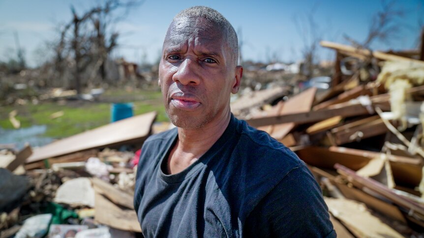 A man in a t-shirt stands in the rubble of his home 